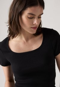 Juoda giliame t-shirt su trumpomis rankovėmis ir plačiu kvadratiniu iškirpimu. Pasižymi prigludusia siluetu ir lygaus tekstūra.