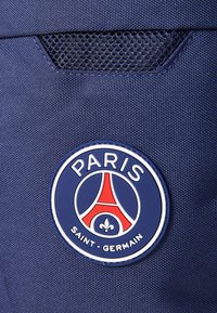 Tela azul marino con un acabado texturizado, que presenta una placa circular de plástico con la Torre Eiffel y "PARIS SAINT-GERMAIN" en rojo y blanco.