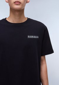 T-shirt en coton noir avec un petit logo blanc imprimé sur la poitrine gauche, col rond et manches courtes. Texture lisse.