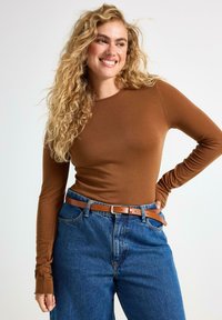Brun långärmad topp i ribbat tyg, kombinerad med högmidjade blå denimjeans och ett brunt skärp i läder.