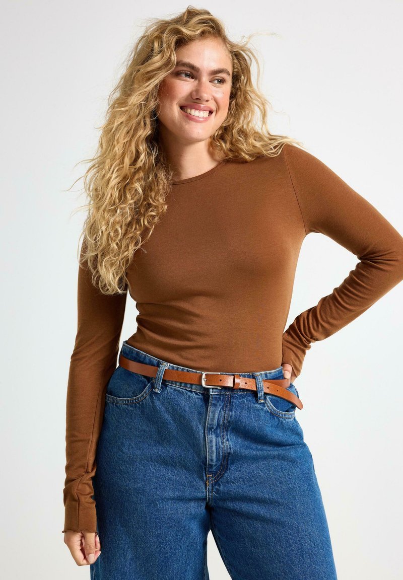 Brun långärmad topp i ribbat tyg, kombinerad med högmidjade blå denimjeans och ett brunt skärp i läder.