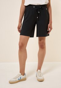 Shorts noirs avec une taille élastique et des détails à cordon de serrage. Assortis à des baskets blanches avec des accents bleus et une semelle texturée.
