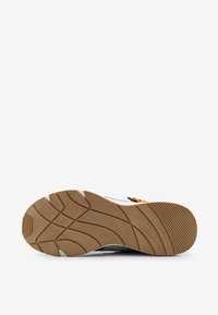 Zapatilla deportiva con una suela de goma texturizada de color marrón y un patrón en zigzag. El material superior es mixto, con acentos en gris y naranja.