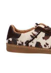 Zapatillas con estampado de vaca, con un upper suave y texturizado, acentos de cuero marrón, suela de goma beige y cordones marrones. Presenta un forro interior marrón.