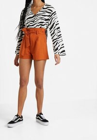 Halenka s dlouhým rukávem s černobílými pruhy zebra, doplněná oranžovými šortkami s vysokým pasem a černými teniskami s bílými tkaničkami.