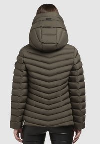 Pūtējs olīvzaļš jaka ar augstu apkakli, ķīļveida quiltu un noņemamu kapuci. Raksturo gluda tekstūra un pieguļošs siluets.