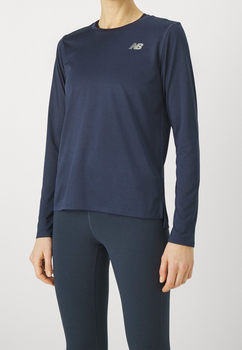 Długi rękaw sportowej bluzki w ciemnym granacie, wykonanej z gładkiej tkaniny, z okrągłym dekoltem i małym logo na piersi. Teksturowana powierzchnia z bocznymi rozcięciami.