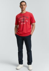 Rød bomulds T-shirt med grafisk tryk, rund hals; kombineret med mørkeblå bukser og hvide sneakers. Simpelt design, afslappet pasform.