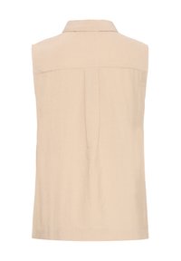 Chemise sans manches beige avec col, présentant un tissu texturé subtil et un pli central au dos pour faciliter les mouvements.