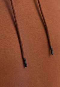 Brown hoodie fabric close-up, featuring textured surface and dark drawstrings with black aglets. Simple, without additional patterns or embellishments.