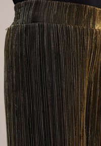 Metalliska veckade byxor i svart och guld. Har vertikala ränder med en silkeslen textur och ett elastiskt midjeband.