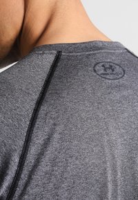 Graues Sportshirt mit glatter Textur, rundem Ausschnitt, schwarzen Nähten und einem kreisförmigen Logo auf der Rückseite in der Nähe des Halses.