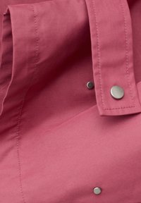 Close-up van roze stof met zichtbare stiksels en drie zilveren drukknopen op een gevouwen manchetgedeelte.
