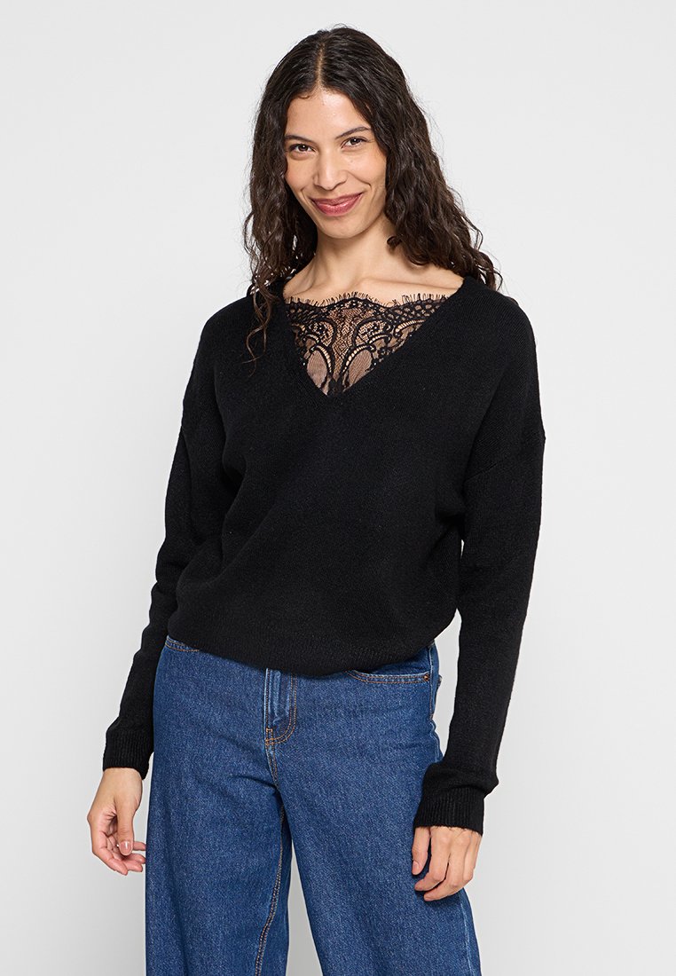Maglione nero con scollatura a V e dettagli in pizzo sul collo. Tessuto morbido, maniche lunghe, abbinato a jeans blu a vita alta.
