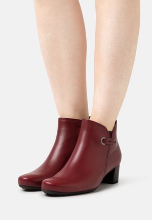 Burgundy nahka nilkkurit, joissa on pyöreä kärki, matala lohkoepä ja koristeellinen metallisilmukka sivulla. Sujuva pinta.