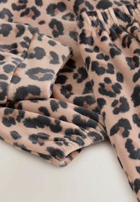 Fleece-fabric leopard print, joka sisältää pehmeän tekstuurin mustilla ja ruskeilla täplillä vaalean beige taustan päällä, esittelee käännettyjä hihoja ja elastisen vyötärön.