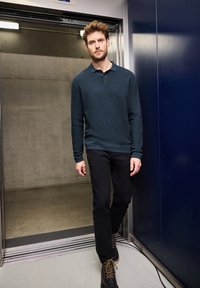 Dunkelblauses Langarm-Polohemd mit strukturiertem Muster, zwei-Knopf-Blende, kombiniert mit schwarzen Slim-Fit-Hosen und braunen Stiefeletten.