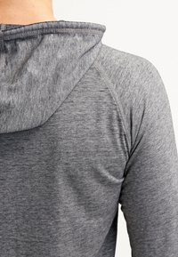 Felpa grigia con cappuccio caratterizzata da un tessuto strutturato, maniche raglan e cappuccio cucito. Messa a fuoco sulla superficie liscia e sul motivo sottile.