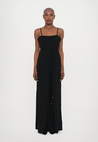 Black, sleeveless maxi dress with a square neckline, slender straps, and a tied waist detail. Soft fabric with a flowing silhouette.