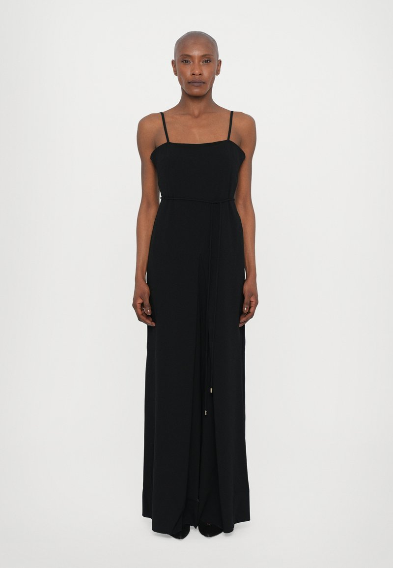 Black, sleeveless maxi dress with a square neckline, slender straps, and a tied waist detail. Soft fabric with a flowing silhouette.