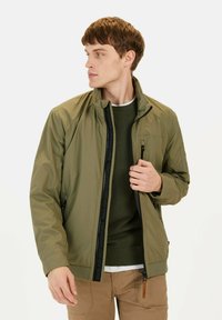 Olivgrüne Jacke mit einem Reißverschluss vorne, Stehkragen und schwarzen Akzenten. Verfügt über Seitentaschen und eine glatte, leichte Textur.