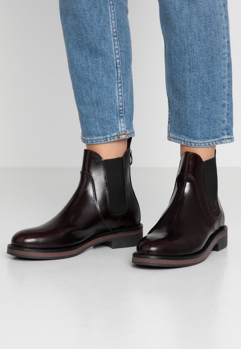 Botas de tobillo de cuero marrón con paneles laterales elásticos, punta redondeada y suela plana. Cuenta con una lengüeta en la parte posterior para facilitar su puesta.