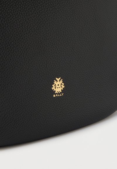 Μαύρη δερμάτινη τσάντα χειρός με υφή, που διαθέτει ανάγλυφο χρυσό λογότυπο στο μπροστινό μέρος. Στρογγυλεμένο σχήμα με μινιμαλιστικό σχεδιασμό.