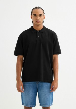 Polo negro de manga corta con cuello, que cuenta con dos botones y un pequeño logo, combinado con pantalones cortos de denim azul claro. Textura suave.