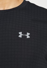 Černé sportovní tričko s přiléhavým střihem, texturovaným vzorem, kulatým výstřihem a malým bílým logem Under Armour na hrudi.