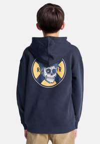 Sudadera azul marino con un gran gráfico en la parte posterior que presenta una calavera con una gorra, enmarcada por un diseño circular amarillo y azul.