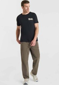 Camiseta negra con gráfico de "Sonríe" en el pecho, combinada con pantalones cargo de cuadros beige que presentan bolsillos grandes y un ajuste holgado.