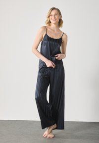 Set di pigiama in satin navy con spalline sottili, caratterizzato da righe verticali, pantaloni larghi e texture liscia.