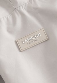Chaqueta marrón con una textura suave y un diseño de tela fruncida. Presenta una etiqueta de goma gris claro con "LARKSON HAMBURG" en letras blancas.