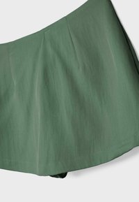 Jupe verte taille haute en ligne A avec coutures discrètes, texture de tissu douce et légères rides sur un fond clair.