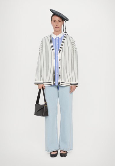 Cardigan oversized rayé en blanc et noir, superposé sur une chemise rayée bleue, associé à un jean bleu clair et des chaussures noires. Béret noir et sac à main.