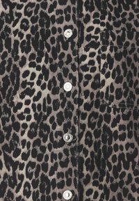 Hemd mit Knöpfen aus einem leichten Stoff, versehen mit einem schwarz-beigen Leopardenmuster, mit silbernen Druckknöpfen und einer Brusttasche.