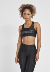 Svart sport-BH med "HUMMEL"-logotyp, med en åtsittande design och breda axelband, tillsammans med högmidjade svarta leggings, båda i slät textur.
