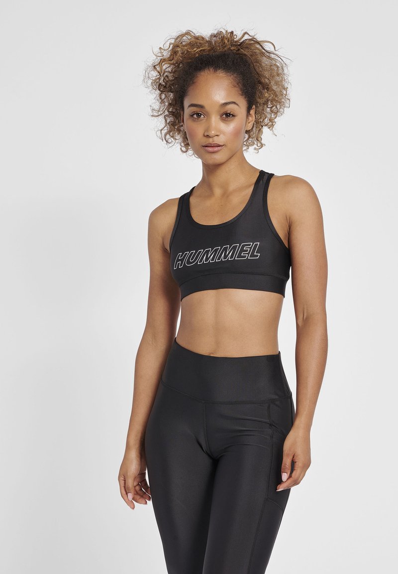 Svart sport-BH med "HUMMEL"-logotyp, med en åtsittande design och breda axelband, tillsammans med högmidjade svarta leggings, båda i slät textur.