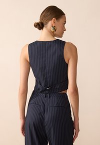 Marinblått ripsrandigt kort topp med en slank design och detaljerad bakknut, i kombination med högmidjade byxor med bakfickor.