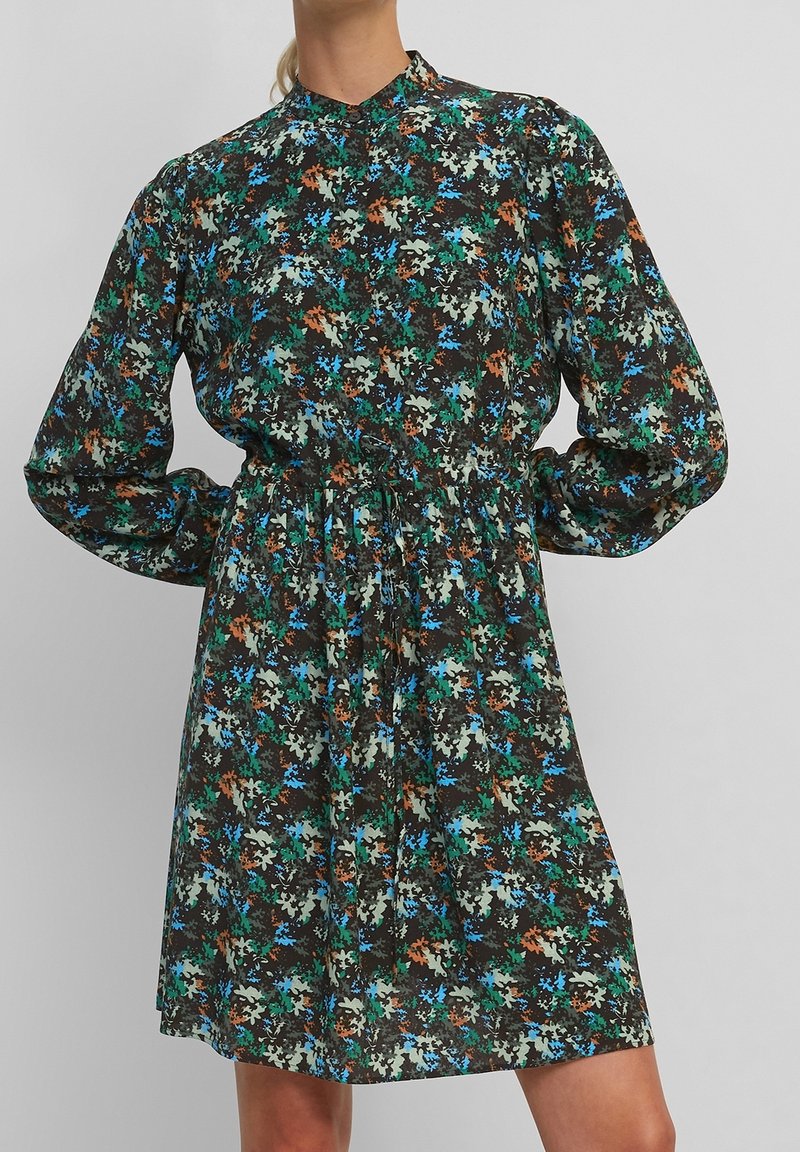Vestido floral con un fondo negro, que presenta patrones en azul, verde y marrón. Manga larga, cintura fruncida y un cuello alto.
