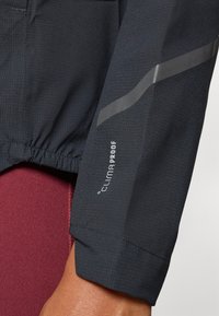 Crna sportska jakna s rukavima od teksturiranog materijala, reflektirajućim detaljima i "CLIMAPROOF" oznakom blizu manšete.