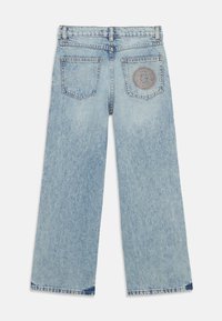 Jeans de tiro ancho en color azul claro, confeccionados en denim, con corte recto, cinco bolsillos y un parche decorativo en el bolsillo trasero derecho.