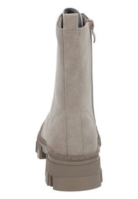 Bottine cheville en suède beige avec une finition lisse et texturée, fermeture éclair et une semelle en caoutchouc robuste. Présente un petit talon et des détails de couture minimaux.
