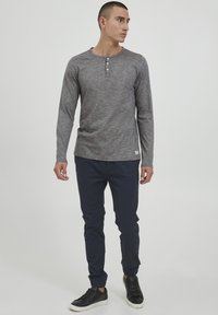 Grå langærmet henley skjorte med tre knapper, parret med marineblå tapered bukser og sorte sneakers. Glat tekstur, afslappet pasform.