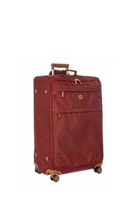 Valise en tissu rouge avec une poignée rétractable, deux roulettes et une poche zippe à l'avant. Présente des accents marron et des supports de base ronds.