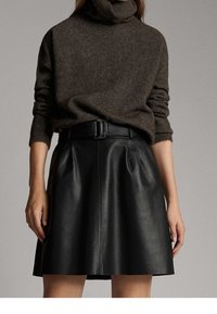 Brun turtleneck sweater parret med en sort lædernederdel med folder og et matchende bælte, der viser en glat struktur og en tætsiddende pasform.