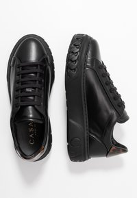 Baskets en cuir noir avec une finition lisse, à lacets, semelle en caoutchouc et un détail distinctif en forme de chaîne sur le côté.