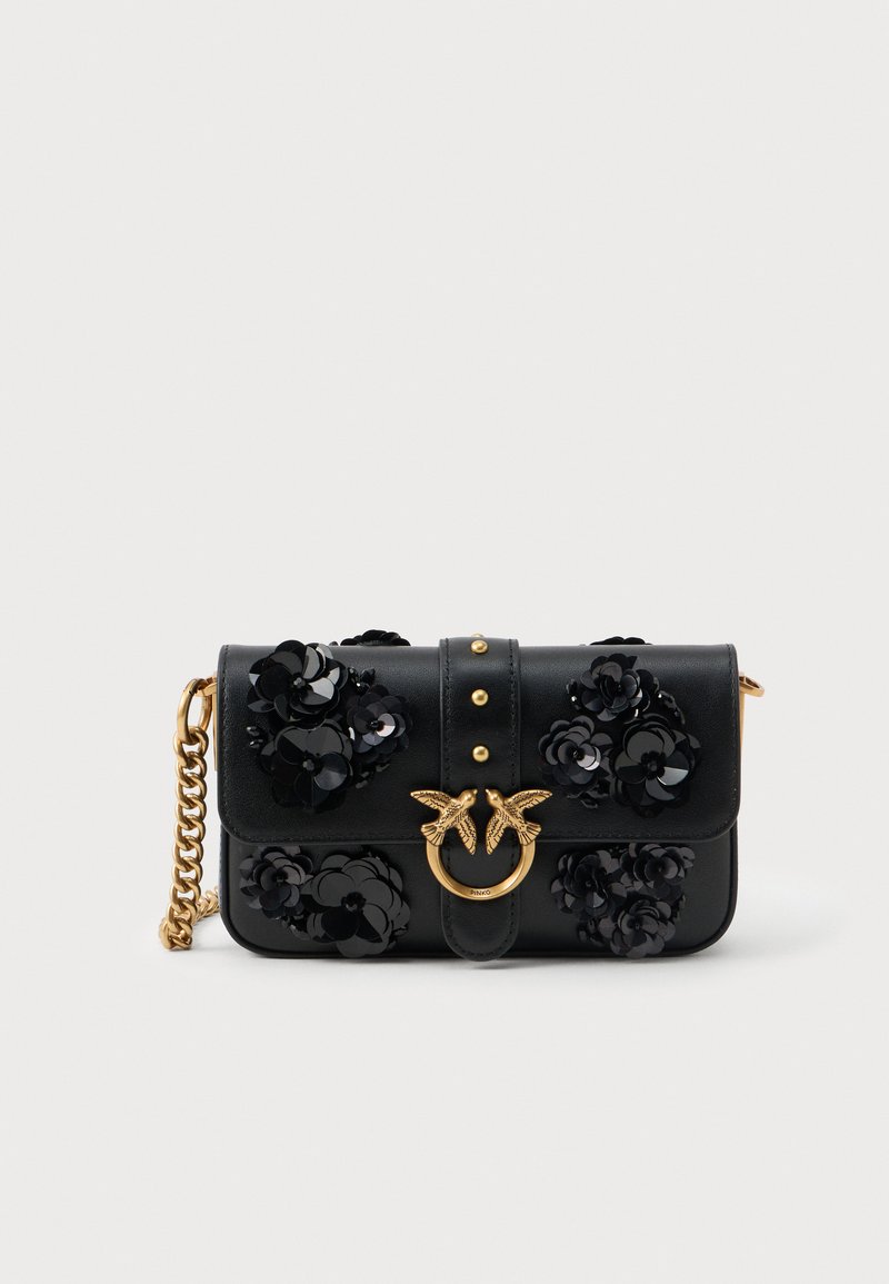 Clutch de couro preto com embellishments florais pretos, fecho de pássaro dourado e alça de corrente dourada sobre um fundo branco.