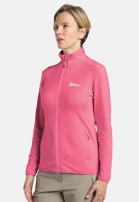 Veste zippée rose en tissu texturé, avec col montant et poches latérales. Présente un logo sur la poitrine gauche.