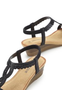 Black wedge sandals with textured straps, embellished with small beads, and a cushioned, brown footbed for comfort.